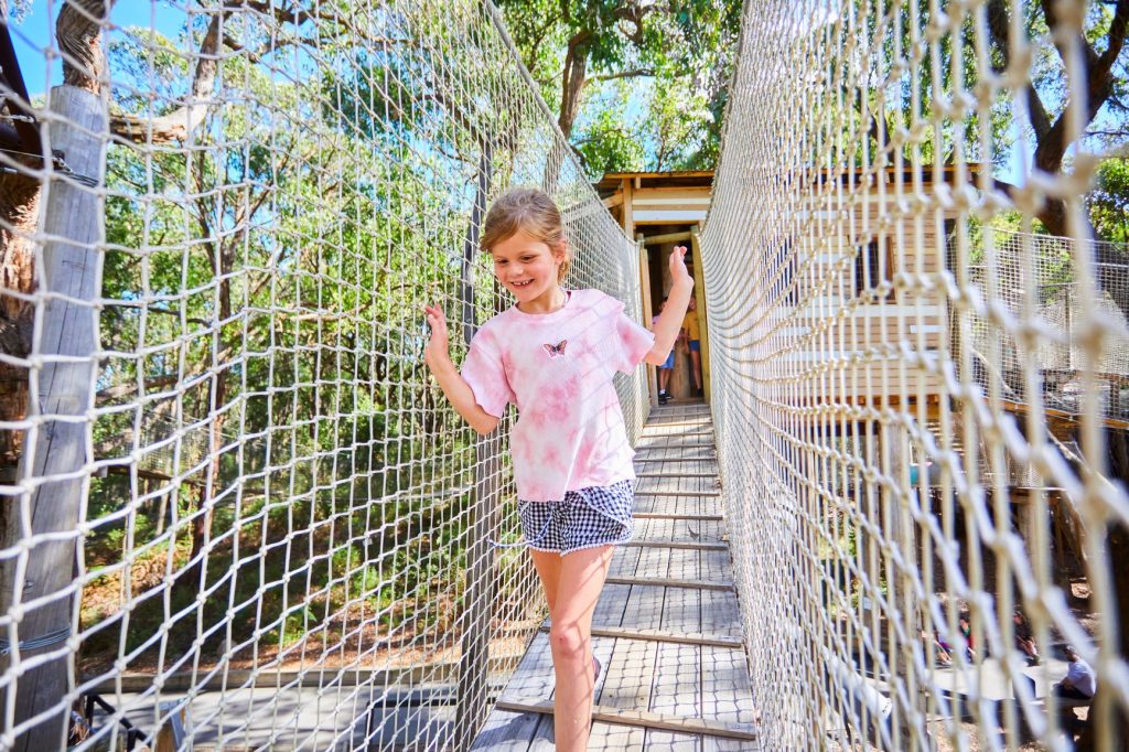 Young girl excitedly walking across enclosed bridge on the Sky Scramble attraction at Enchanted Adventure