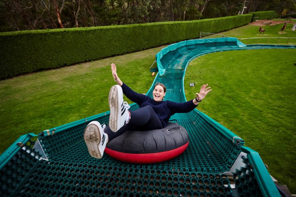 Woman going backwards down one of the curly Tube Slides with arms in the air at Enchanted Adventure
