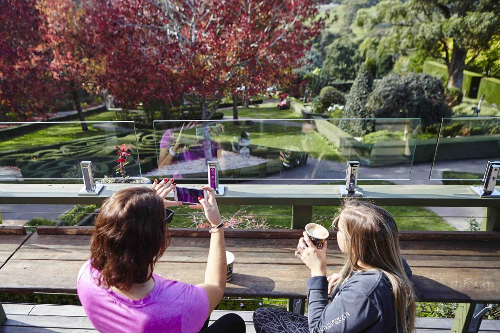 Two women enjoying coffee and taking photos on the Cafe balcony overlooking formal gardens in Autumn