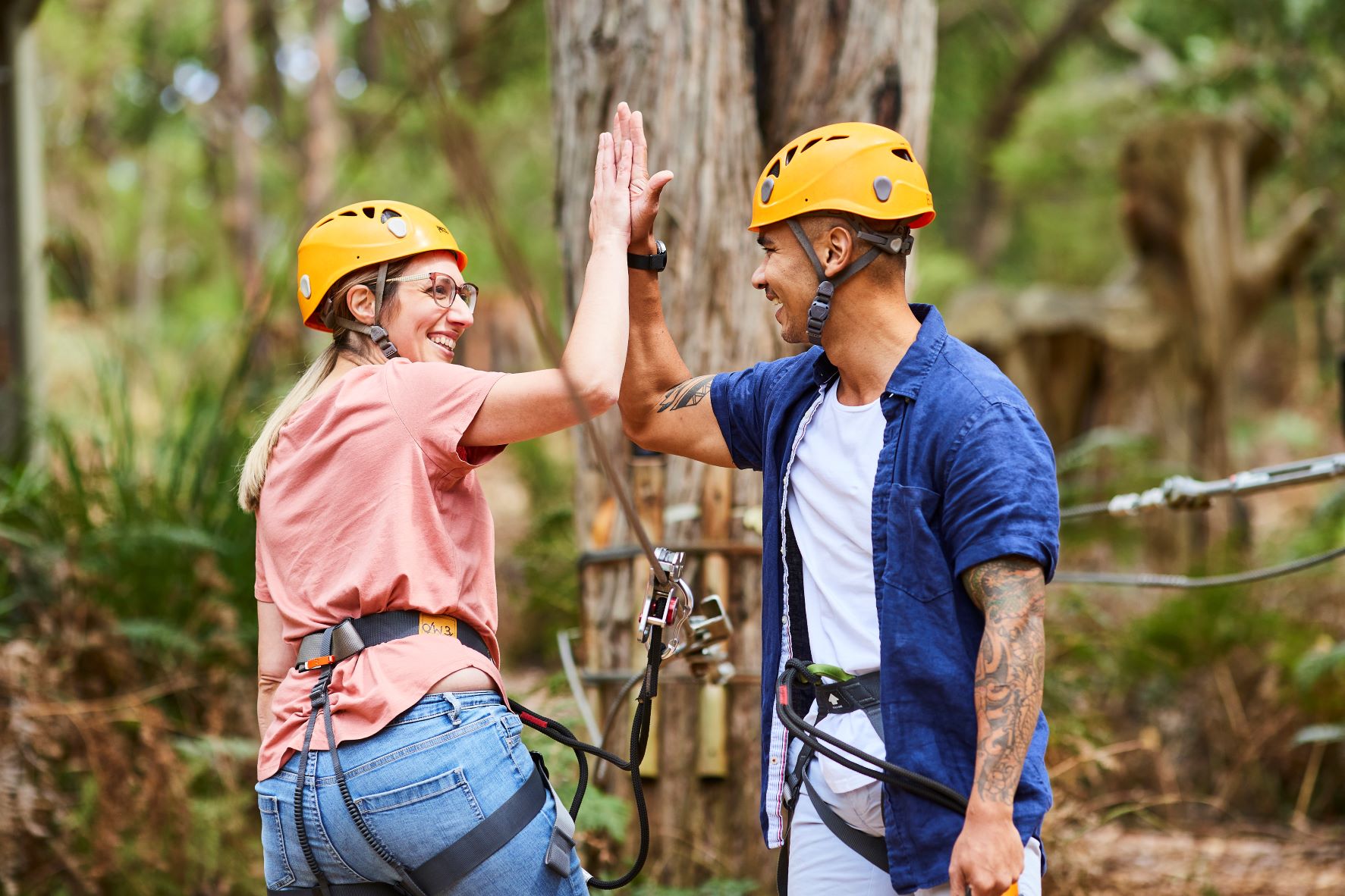 Two adults high fiving after finishing a zipline on the Grand Tree Surfing course